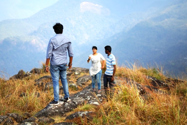 Woman pointing at man on mountain top with another man looking on
